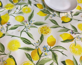 May include: White tablecloth with a vibrant lemon pattern. The design features yellow lemons, lemon slices, green leaves, and small blue flowers. A white plate rests on the tablecloth, suggesting a dining setting.