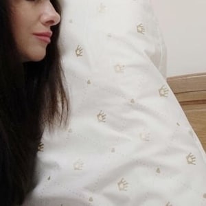 以下が含まれることがあります： 金色の王冠模様の白い枕カバー。枕カバーは木製のヘッドボードのあるベッドの上にあります。