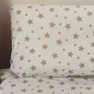 May include: White bedding with a light brown star pattern. The bedding includes a pillowcase and a fitted sheet.
