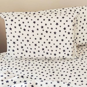 Puede incluir: Bedding blanco con un patrón de estrellas azul marino. La ropa de cama incluye una sábana bajera, una sábana plana y dos fundas de almohada.