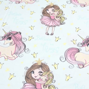 May include: A light blue fabric with a repeating pattern of pink unicorns, princesses, crowns, and stars. The text "Believe in Magic" is repeated throughout the pattern.