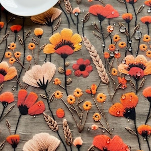 May include: A close-up of a tablecloth with a floral pattern. The tablecloth is a light brown colour with orange, red, and yellow flowers. There are water droplets on the tablecloth.