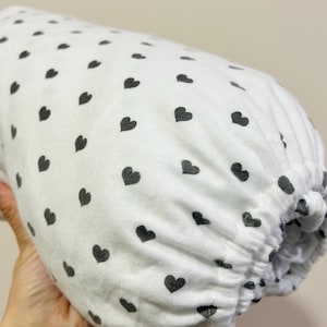 Puede incluir: Sábana bajera blanca con un patrón de corazones negros.