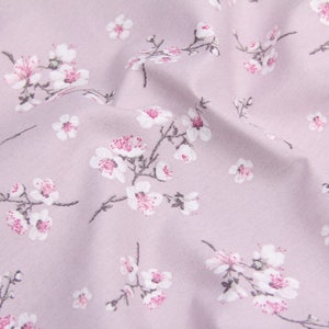 以下が含まれることがあります： 薄い紫色の生地のクローズアップ。白とピンクの花柄がプリントされています。生地は柔らかく、上品な光沢があります。