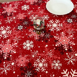 May include: Red tablecloth with a white snowflake pattern. A small snow globe with a Santa Claus figurine is on the table. A white plate is on the table.