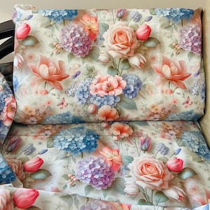 Pode incluir: Uma almofada com padrão floral sobre um fundo bege claro. A almofada apresenta uma variedade de flores, incluindo rosas, hortênsias e tulipas em tons de rosa, azul e roxo.