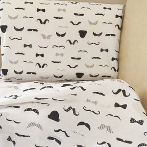 May include: White bedding with a black and white pattern of mustaches, bowties, and hats.