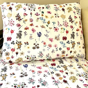 May include: A white pillowcase with a floral pattern featuring a variety of colorful flowers. The pillowcase is made of soft, comfortable fabric and is perfect for adding a touch of elegance to any bedroom.