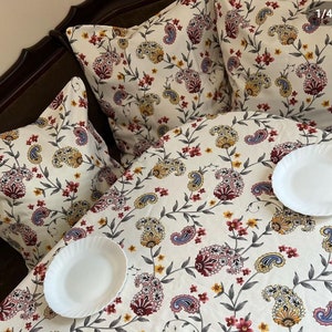 May include: A white tablecloth with a paisley pattern in shades of red, blue, yellow, and green. Two white plates are on the tablecloth.