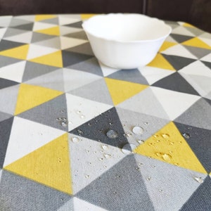 Puede incluir: Primer plano de una tela con estampado geométrico amarillo y gris con gotas de agua en la superficie. La tela es impermeable y resistente a las manchas.