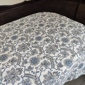 May include: A white tablecloth with a blue and gray floral pattern. The tablecloth has a damask design with intricate details.