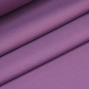 May include: A close-up of a smooth, soft, purple fabric. The fabric is folded in half, showing the texture and color.
