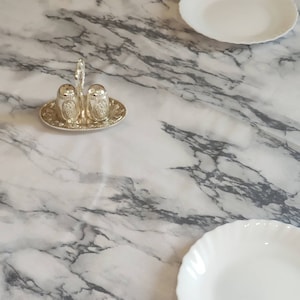 May include: Two silver salt and pepper shakers with a decorative design on a silver tray on a white marble table top.