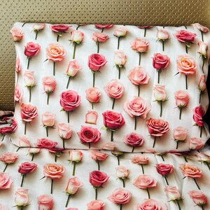 May include: A white pillowcase and matching bed sheet featuring a repeating pattern of individual pink and peach roses. Each rose is depicted with green stems and leaves, arranged in a grid-like layout across the fabric surface.