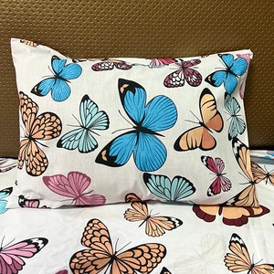 May include: White pillowcase and bedding set with a repeating pattern of colourful butterflies. The butterflies are in shades of blue, pink, orange, and purple, with black detailing. The background is white.