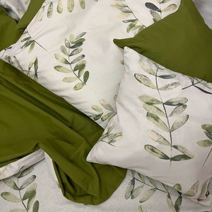 May include: A set of bedding featuring a white background with green leafy patterns. The bedding includes a pillowcase, a flat sheet, and a fitted sheet. The pillowcase and flat sheet have a white background with green leafy patterns. The fitted sheet is solid green.