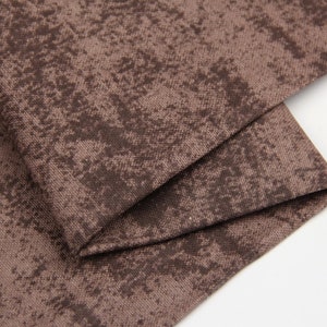 May include: Close-up of a brown fabric with a subtle, textured pattern. The fabric has a slightly distressed look, giving it a vintage feel.