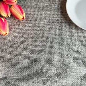 May include: A white ceramic plate sits on a grey textured tablecloth with a bouquet of pink and yellow tulips.