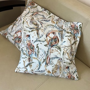 Puede incluir: Dos almohadas decorativas con fondo blanco y un patrón colorido de pájaros y follaje.