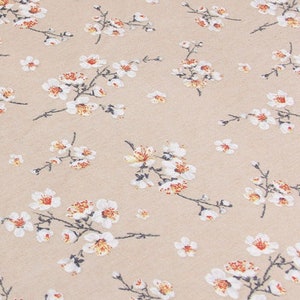 以下が含まれることがあります： ベージュの生地に白い花の模様が施されています。花は小さく繊細で、薄い茶色の中心があります。