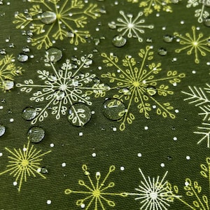 Op de afbeelding: Een donker olijfgroene stof met een herhalend patroon van witte en lichtgele lijntekeningen van sneeuwvlokken. Talrijke heldere waterdruppels zijn verspreid over het oppervlak van het textiel, wat zorgt voor een getextureerd uiterlijk.