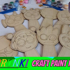 May include: A collection of unfinished wooden character cutouts featuring various cartoon-style faces, including figures with headphones, horns, and bows. The set includes small paint pots and blue-handled brushes for crafting projects.