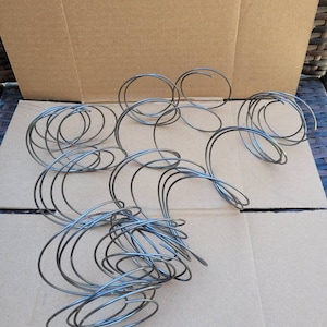 May include: A set of 10 silver metal wire coils, arranged in a random pattern on a brown cardboard surface.