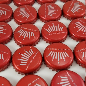 May include: A collection of red bottle caps with the words "King of Beers" and a white crown design.