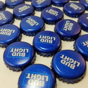May include: A collection of blue Bud Light bottle caps with white lettering. The caps are arranged in a circular pattern.