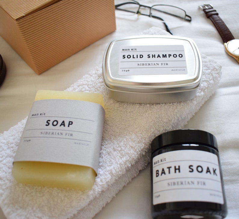 May include: A set of bath and body products in a Siberian Fir scent. The set includes a bar of soap, a tin of solid shampoo, and a jar of bath soak. All products are labeled with the text "Man Kit" and "Siberian Fir".