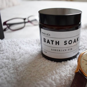 May include: A brown glass jar with a black lid and a white label that reads "Man kit Bath Soak Siberian Fir".