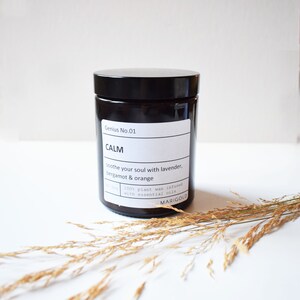 May include: A black glass candle jar with a white label that reads "Genius No. 01 CALM soothe your soul with lavender, bergamot & orange 100% plant wax infused with essential oils MARIGOLD".