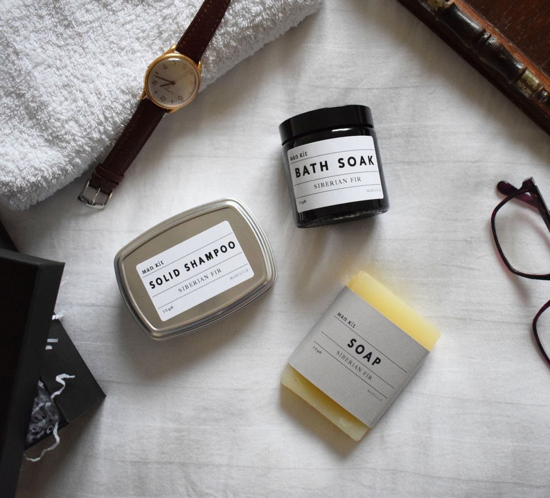May include: A set of three bath products in a Siberian Fir scent. The products include a solid shampoo bar in a silver tin, a bar of soap, and a bath soak in a black jar.