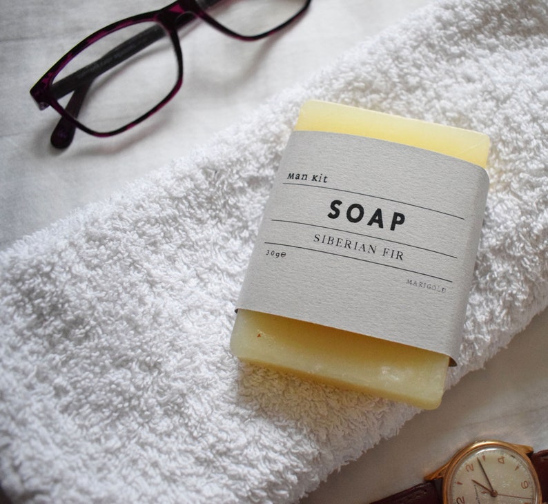 May include: A white bar of soap with a label that reads "Man Kit Soap Siberian Fir 30g Margo & Co."