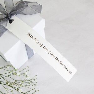 Puede incluir: Una caja de regalo blanca con una cinta gris y una etiqueta de regalo blanca que dice "With lots of love from the Bournes xxx".