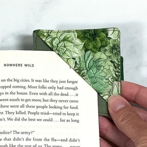 A green succulent fabric corner bookmark being slid over the corner of a page of a book.