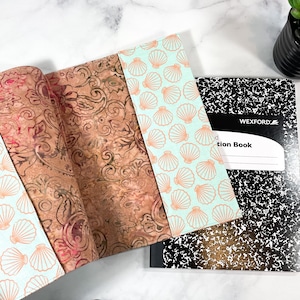 May include: A light blue notebook cover with a seashell pattern, a brown cork notebook with a paisley pattern, and a black and white composition notebook with the text "Wexford Composition Book".