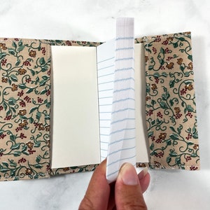 May include: A small, fabric-covered notebook with a floral pattern. The notebook is open, revealing lined paper.