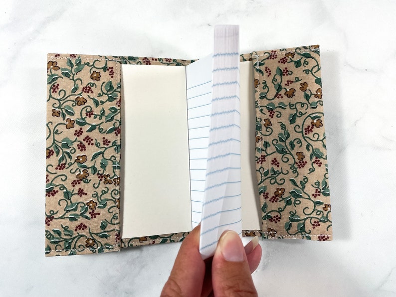 May include: A small, fabric-covered notebook with a floral pattern. The notebook is open, revealing lined paper.