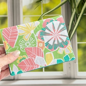 May include: A green fabric wallet with a floral pattern featuring pink, yellow, and teal flowers. The wallet has a teal stitched border.
