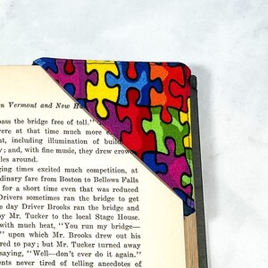 May include: A colorful bookmark with a puzzle piece pattern. The bookmark is folded over the corner of a book with text about Southern Vermont and New Hampshire. The text reads "When staging times excited much competition, at the time the ordinary fare from Boston to Bellows Falls was $3.00, but for a short time even that was reduced to 25 cents. Drivers sometimes ran the bridge to get there first. One day Driver Brooks ran the bridge and was followed by Mr. Tucker to the local Stage House. He exclaimed with much heat, "You run my bridge - the fine is $2," upon which Mr. Brooks drew out his wallet and offered to pay; but Mr. Tucker turned away much calmed, saying, "Well-don't ever do it again." Old residents never tired of telling anecdotes of"