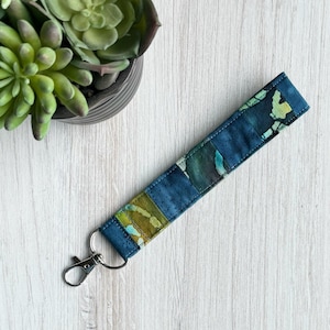 May include: A blue and green patterned fabric key chain with a silver metal key ring.