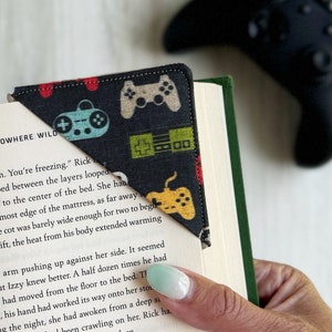 May include: A black and green fabric bookmark with a video game controller design. The bookmark is folded over the corner of a book with the text "NOWHERE WILD" visible.