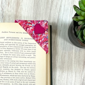May include: A pink and white fabric bookmark with a heart-shaped design. The bookmark is folded over the corner of a book titled "Southern Vermont and New Hampshire". The text on the page reads "EARLIEST SETTLEMENTS IN ROCKINGHAM AND SURROUNDING TOWNS".