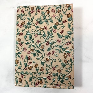 May include: A beige fabric book cover with a repeating pattern of green vines, brown flowers, and red berries.