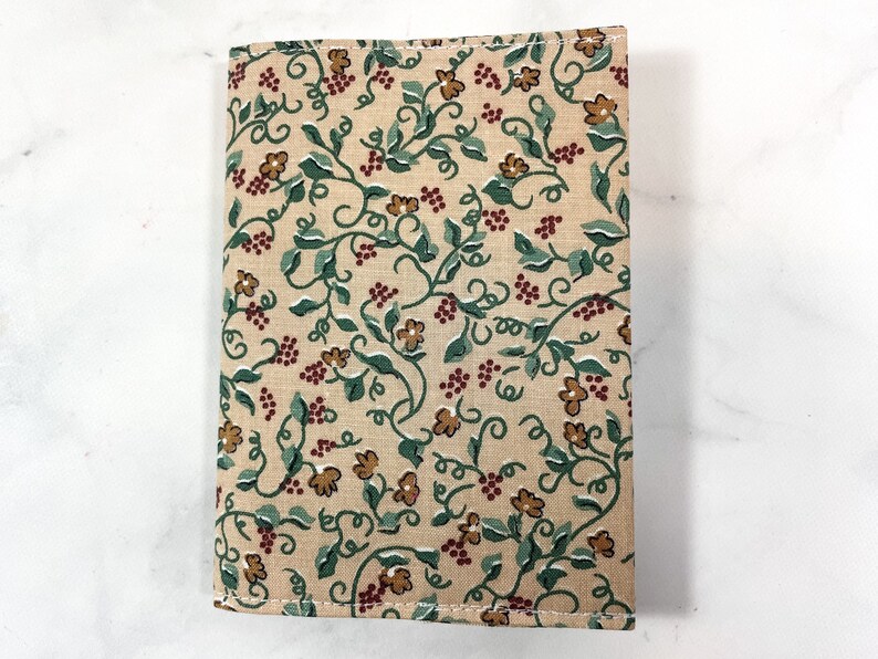 May include: A beige fabric book cover with a repeating pattern of green vines, brown flowers, and red berries.
