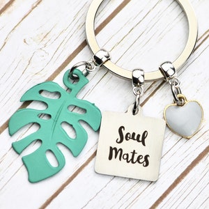 May include: A silver key ring with three charms: a green monstera leaf, a square tag with the text "Soul Mates", and a small silver heart.