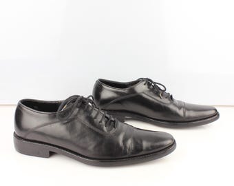 May include: A pair of black leather dress shoes with laces. The shoes have a classic design with a pointed toe and a low heel. The shoes are set against a white background.