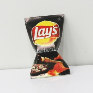 May include: A miniature Lay's Barbecue potato chip bag. The bag is black with the Lay's logo in red and yellow. The word "Barbecue" is printed below the logo. The bottom of the bag features an image of barbecue food.