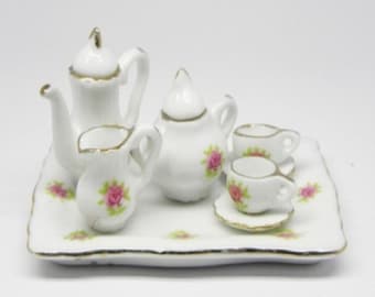 May include: Miniature white porcelain tea set with gold trim and pink rose accents. The set includes a teapot, creamer, sugar bowl, and two teacups with saucers, all arranged on a rectangular tray.